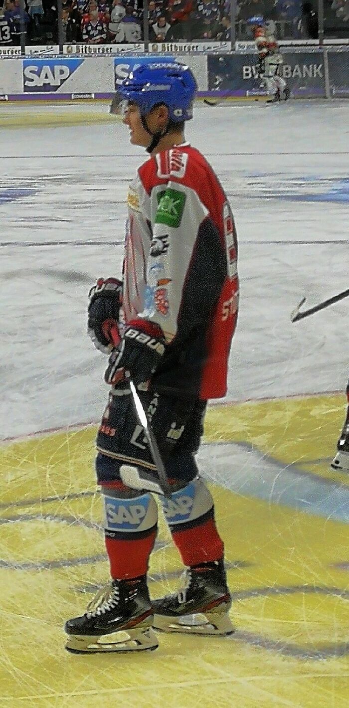 Tim Stützle on ice wearing red and white hockey gear and a blue helmet during a professional game.