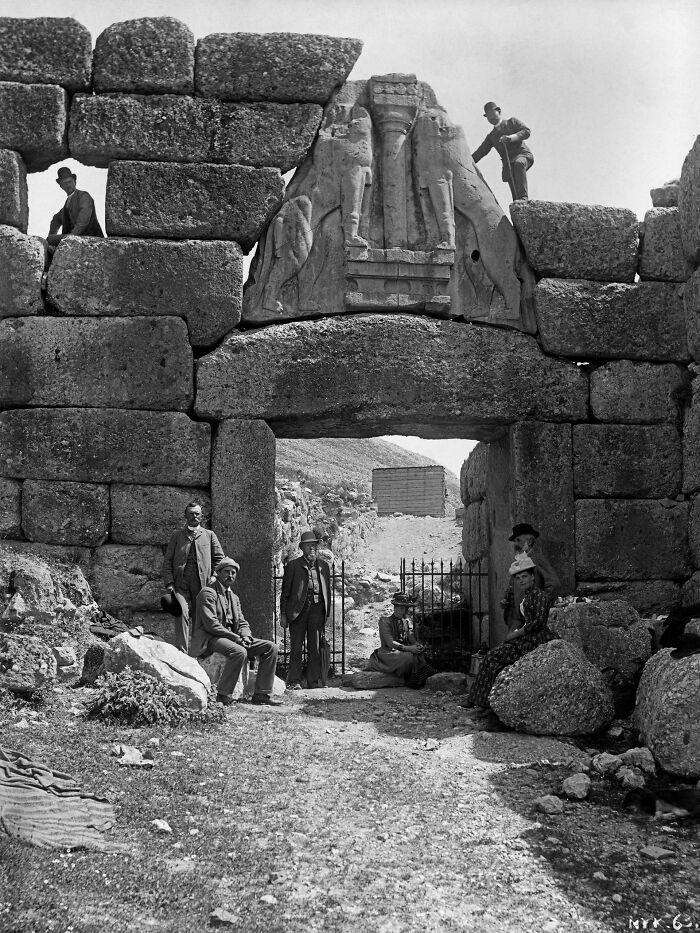 Historic site photo showing ancient stone gateway with carved relief and people exploring the archaeological site.