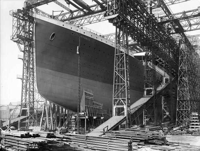 Historic site photo of the Titanic ship under construction inside a large shipyard with cranes and scaffolding.