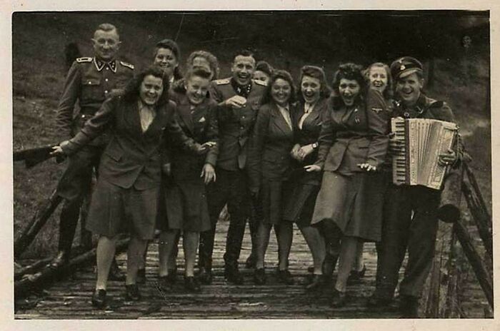 Group of historic site soldiers and women in vintage uniforms posing on a wooden bridge, showcasing history repeated moments.