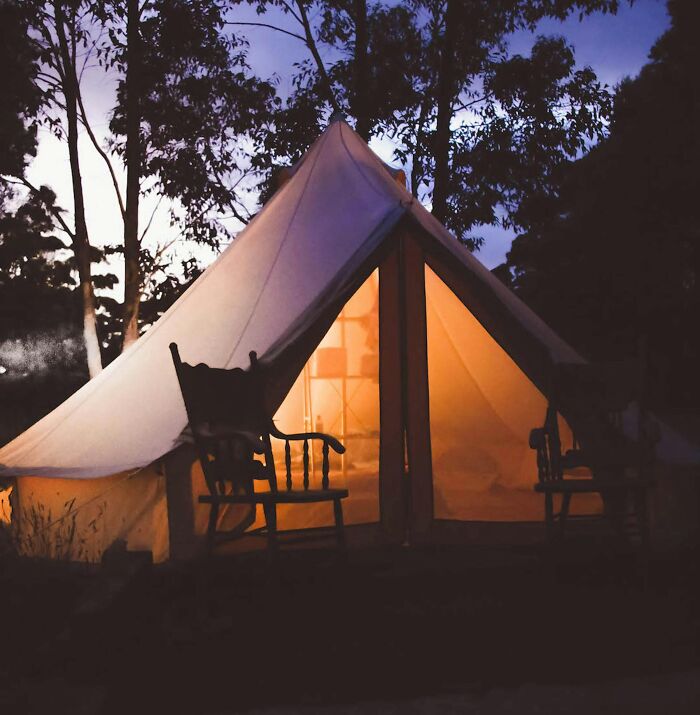 Luxury glamping tent lit warmly at dusk, surrounded by trees, illustrating contrasts in rich people lifestyle statements.