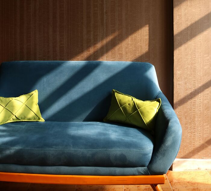 Blue velvet sofa with green pillows in warm sunlight, illustrating luxury and out of pocket statements by rich people.