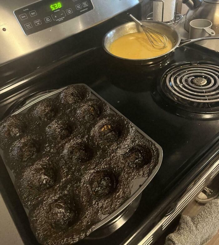 Overburnt muffins in a pan next to a pot with batter on a stovetop, showing a dessert ruined unexpectedly.