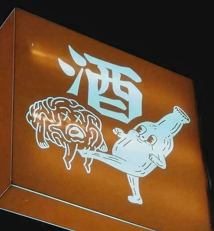 Funny and confusing picture of a cartoon bottle kicking a brain illustration next to Asian characters on a brown sign.