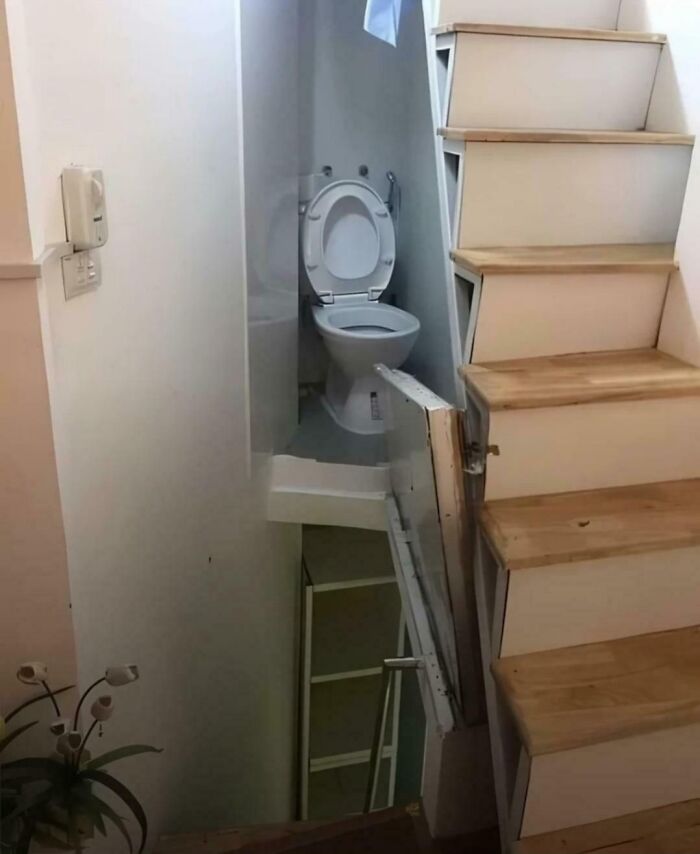 Small toilet placed behind an awkward staircase door illustrating dumb designer decisions creating unexpected problems.