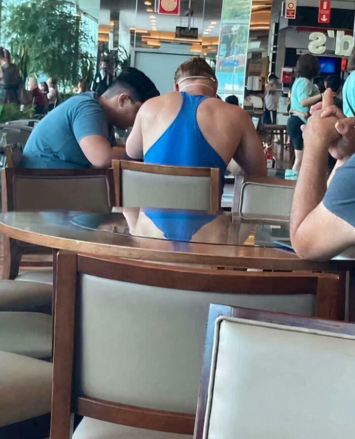 Man in a blue swimsuit sitting at a dining table with others, creating a confusing and funny visual illusion.