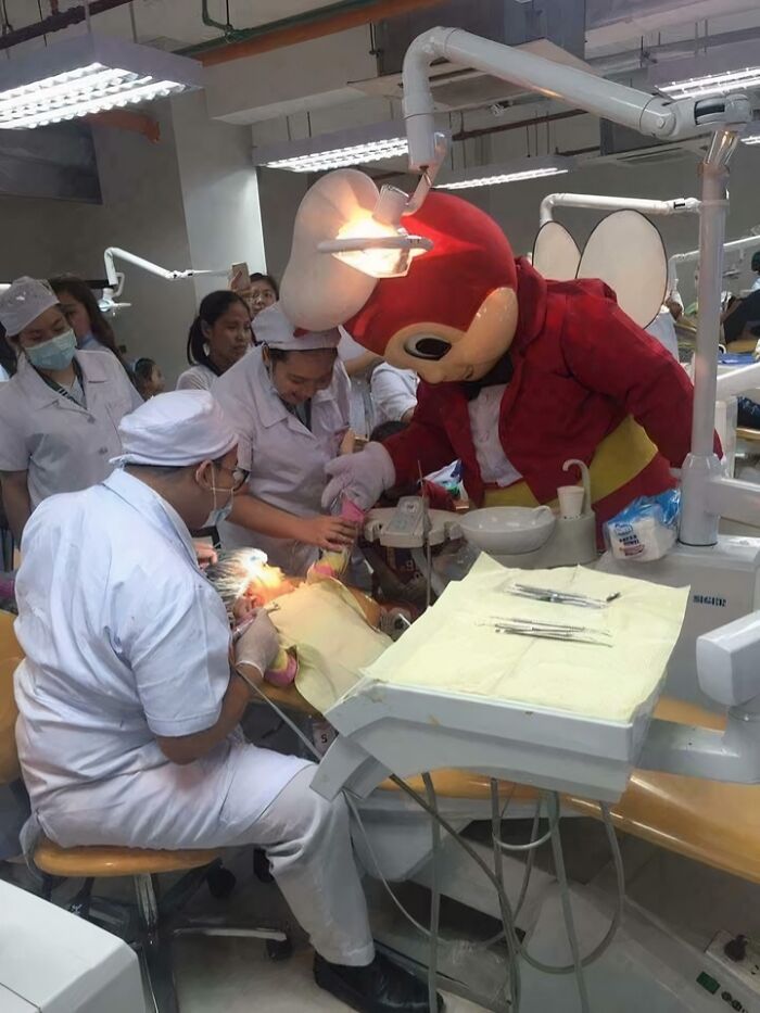 Dental team treating a patient while a person in a large cartoon costume assists in a confusing and funny scene.