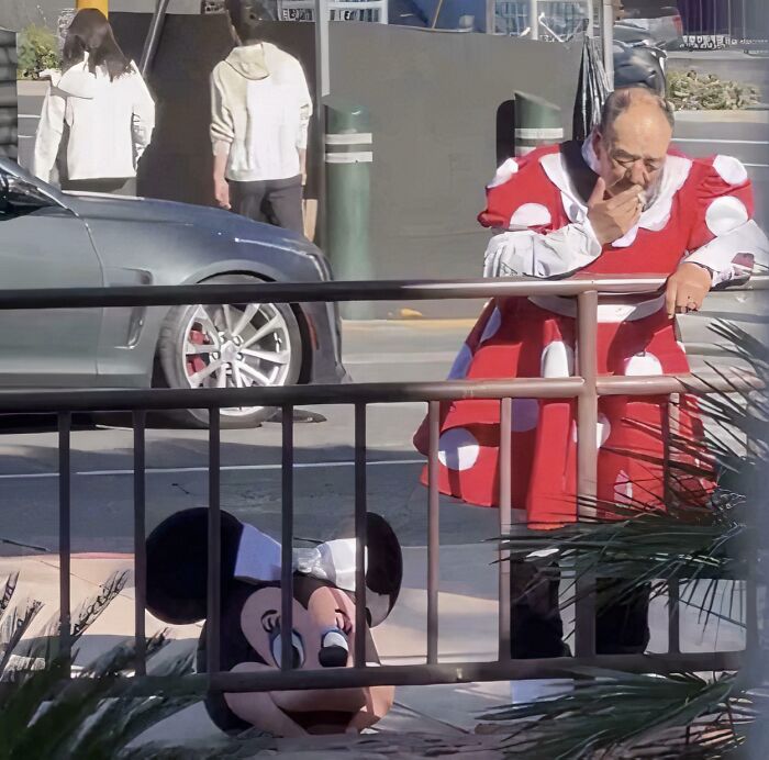 Man dressed in a Minnie Mouse costume head on the ground while another person in a similar outfit stands nearby, confusing scene.