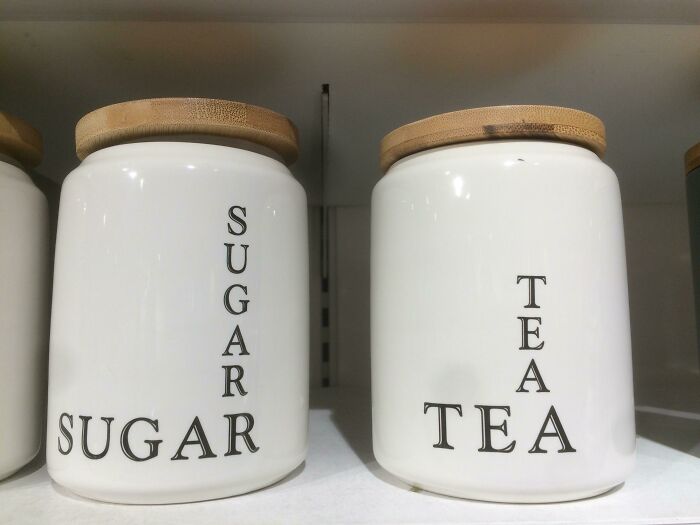 White ceramic jars labeled with vertical and horizontal text displaying sugar and tea, showcasing designers' writing fails.