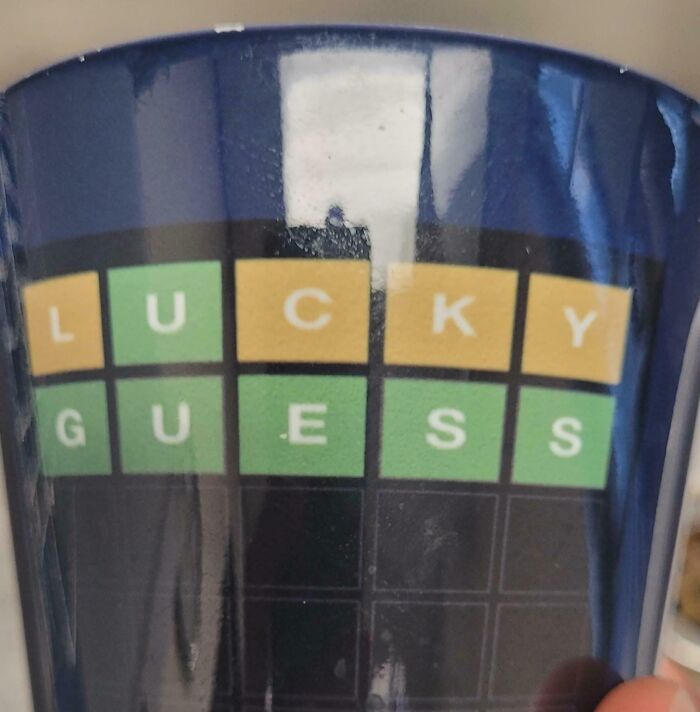 Close-up of a design fail showing a mug with a misspelled Wordle-style game reading LUCKY GUESS.