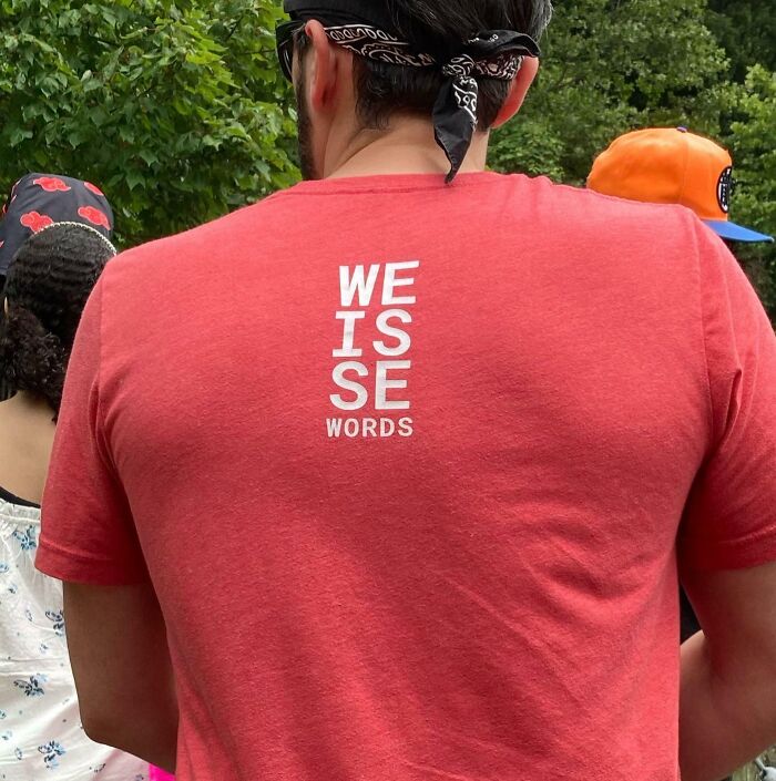Man wearing a red shirt with a failed design of miswritten words, illustrating designers' writing mistakes outdoors.