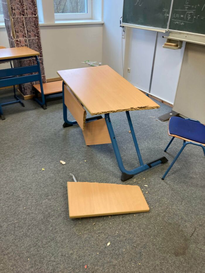 Broken classroom desk with damaged wood and fallen panel, illustrating weirdest teacher behavior witnessed in class.