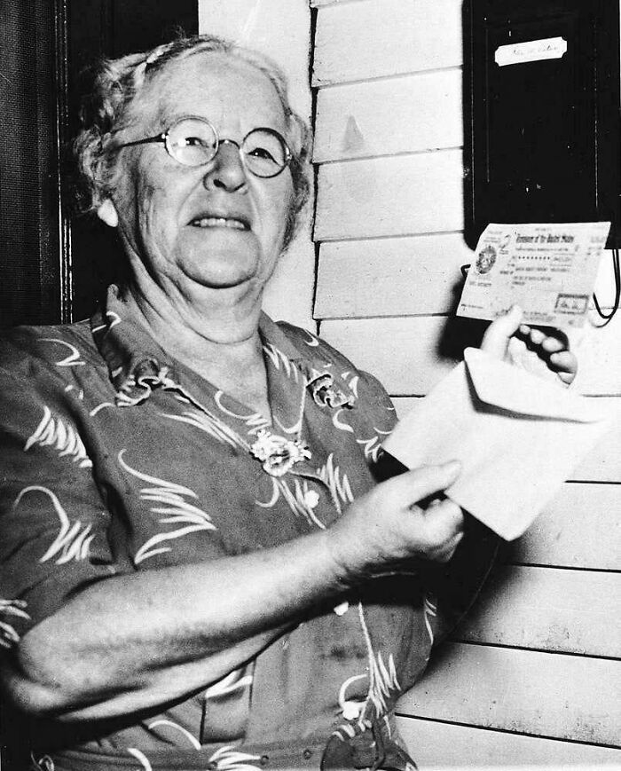 Elderly woman holding a document by a mailbox, a historic US history photo showing life in the past.