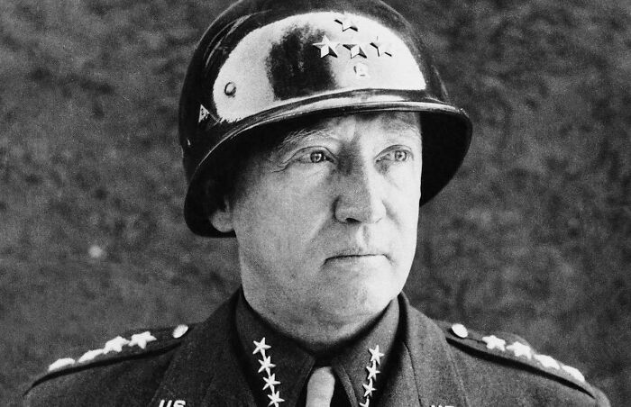 Black and white US history photo of a World War II general wearing a helmet decorated with stars.