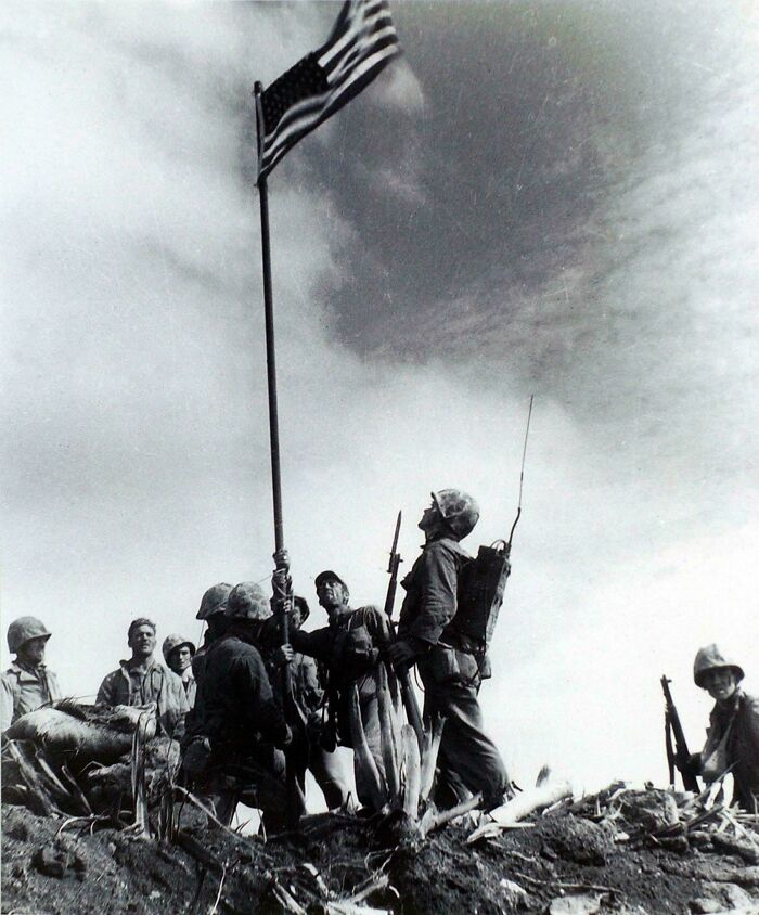 Historic US soldiers raising the American flag during a battle, showcasing a powerful moment in US history photos.