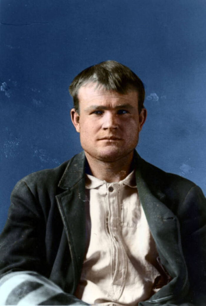 Colorized portrait of a man from US history wearing worn clothing against a plain blue background in a historical photo.