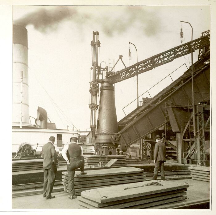 Three men inspecting industrial equipment on a ship deck in a vintage US history photo showing the past.