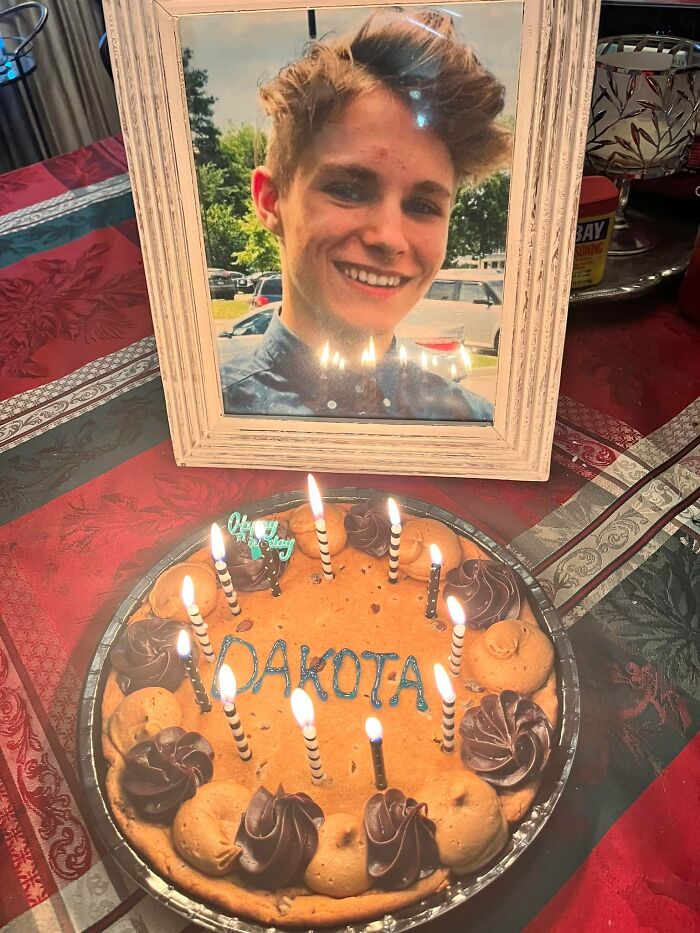 Framed photo of a smiling young man next to a birthday cookie cake with lit candles and the name Dakota.