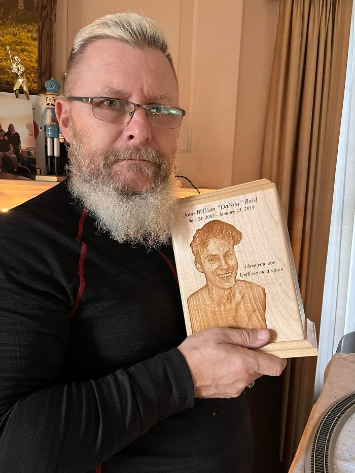 A dad holding a wooden memorial plaque of his late son, connecting with the heartbeat inside a teddy bear.