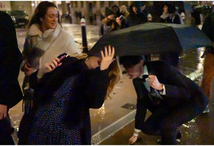 People sharing an umbrella on a rainy street at night, capturing candid moments in street photos by Perry Hall.