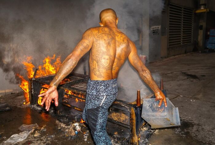 Man with tattoos on his back near a fire on the street, captured in candid street photos by Perry Hall.