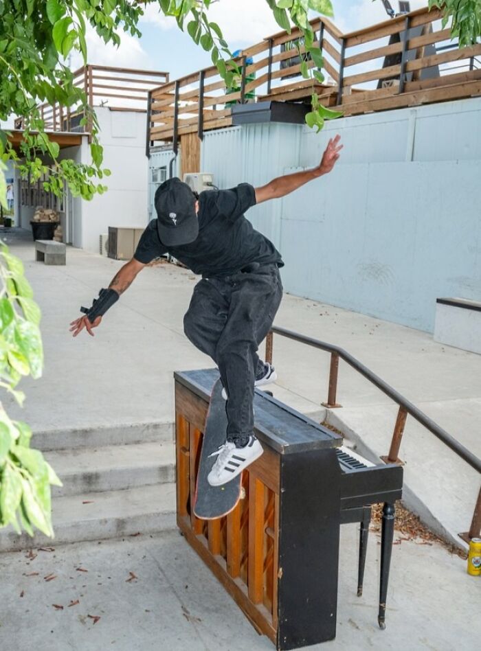 Skateboarder performing trick over a piano in an urban setting, captured in street photos by Perry Hall.