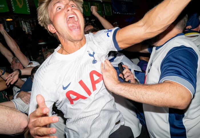Young man in a Tottenham jersey celebrates passionately in a crowded bar, capturing life exactly as it happens in street photos.