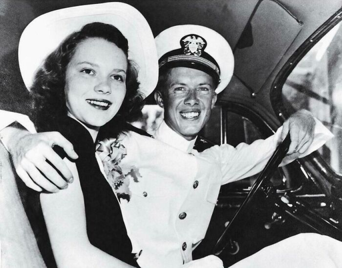 Smiling young couple in a car, man in naval officer uniform, vintage US history photo showing the past uniquely.