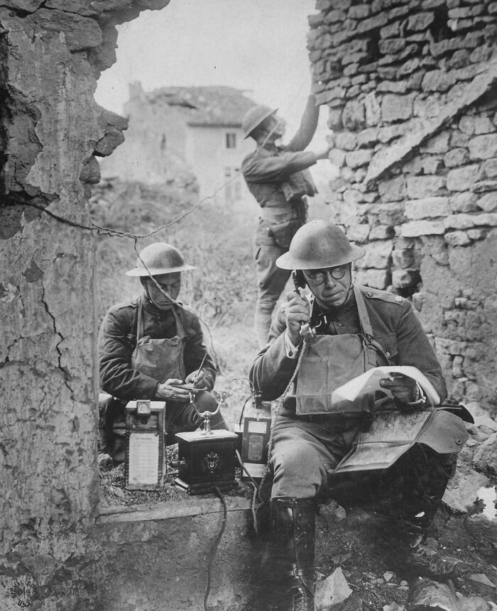 Three soldiers in helmets using old communication equipment amid ruins, a rare US history photo showing wartime technology.