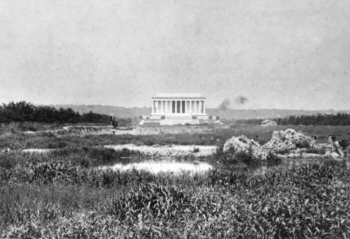 Black and white US history photo showing the Lincoln Memorial under construction amid a grassy field.