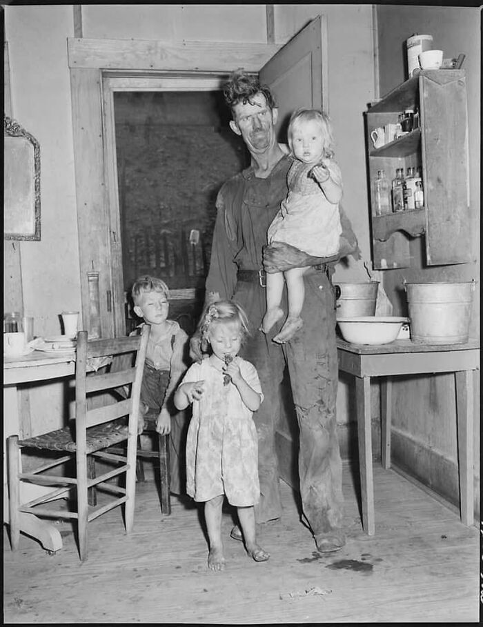 Black and white historical photograph of a man and three children in a modest home depicting a world you'd hardly recognize today.
