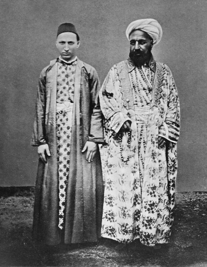 Black and white historical photograph of two men in traditional Middle Eastern robes and headwear standing side by side.