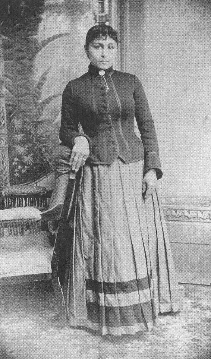 Vintage historical photograph of a woman in 19th-century attire posing indoors, depicting a world you'd hardly recognize today.