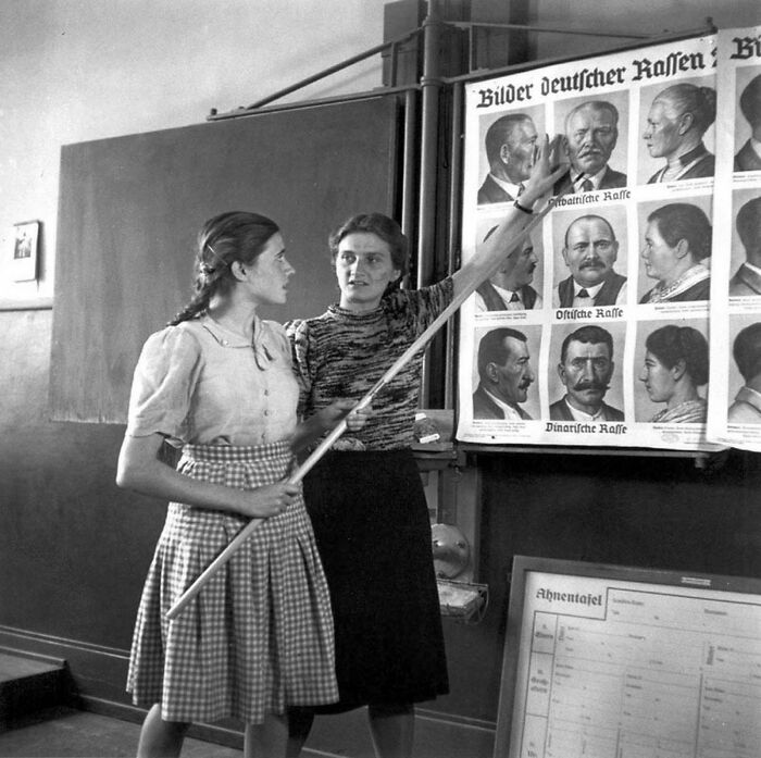 Two women examining a historical race classification poster in a classroom depicting a world you'd hardly recognize today.