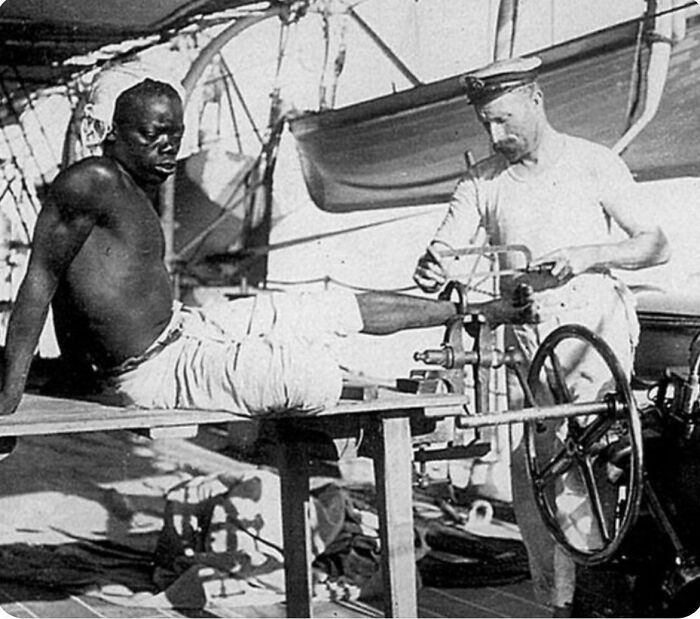 Historical photograph showing a sailor treating a man's injured foot aboard a ship, depicting a world you'd hardly recognize today.