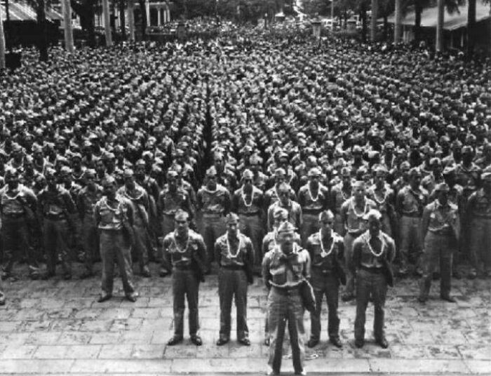 Large group of soldiers standing in formation wearing leis in a historical photograph depicting a world you'd hardly recognize today.