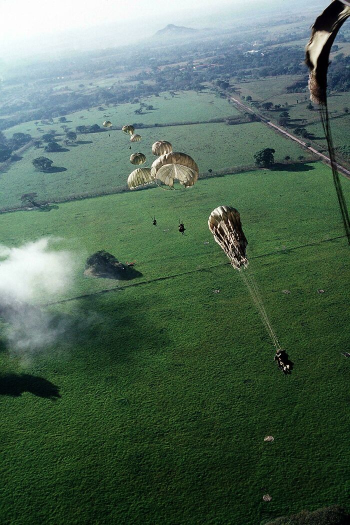 Paratroopers descending with parachutes over green fields in an interesting historical photograph depicting a past world scene.