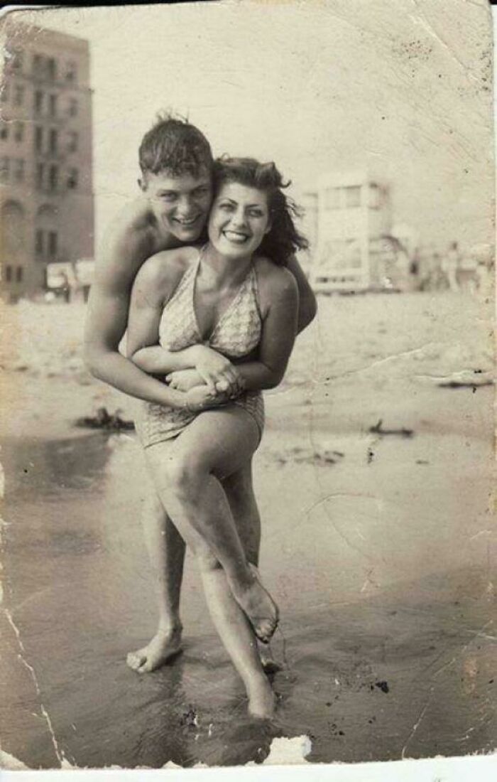Couple smiling and posing playfully on a beach in an old historical photograph depicting a world you'd hardly recognize today.
