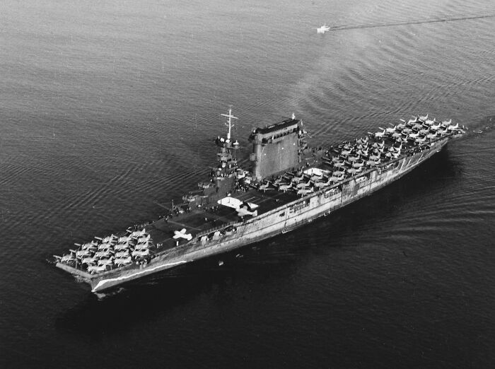Black and white historical photograph of a large aircraft carrier filled with vintage planes at sea.