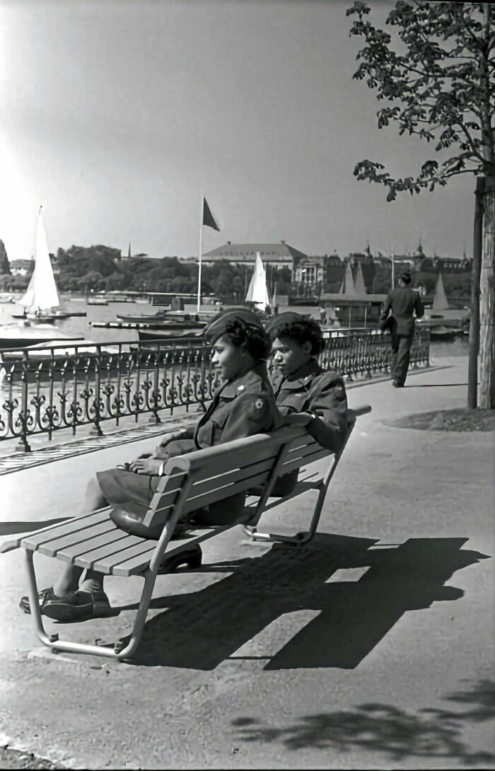 Two women in military uniforms relax on a bench by the waterfront in an interesting historical photograph.