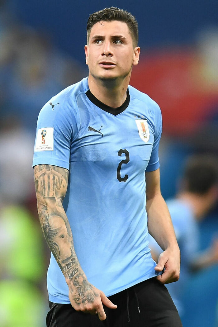 Jos&eacute; Mar&iacute;a Gim&eacute;nez in Uruguay national team jersey during a football match, showing tattoos on his arm.