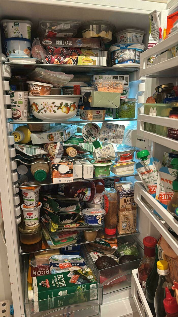 Cluttered fridge contents filled with various food items and drinks, showing interesting and unorganized fridge storage.