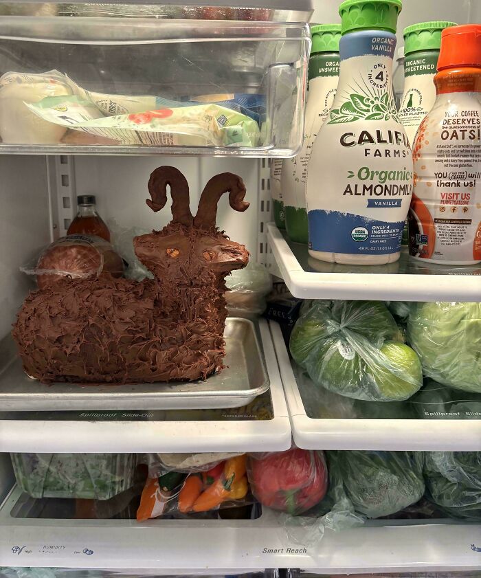 Unusual fridge contents featuring a chocolate sculpture with horns among typical groceries and almond milk bottles.