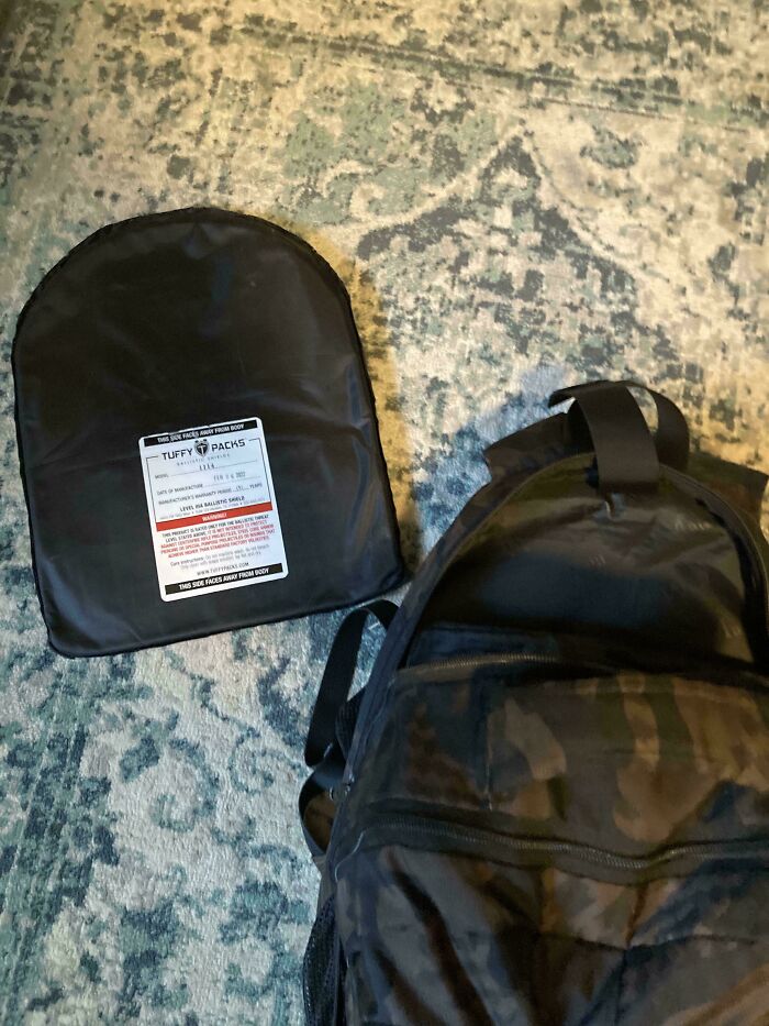 Bulletproof backpack and armor panel laid out on a patterned carpet, highlighting safety gear related to U.S. warning images.