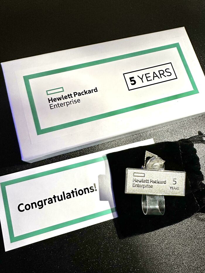 Hewlett Packard Enterprise 5 years pin and congratulations card on a black surface, U.S. warning concept image.