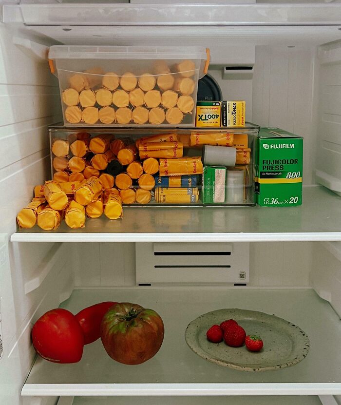 Fridge contents with a collection of vintage film rolls, tomatoes, and strawberries on a plate inside a clean fridge.