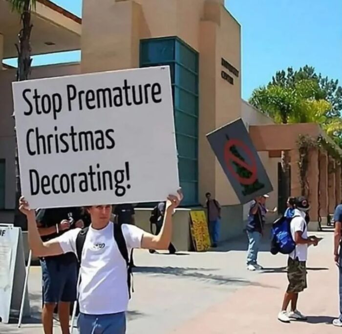 Person holding a sign protesting premature Christmas decorating in a sunny outdoor area, relatable hilarious meme moment.