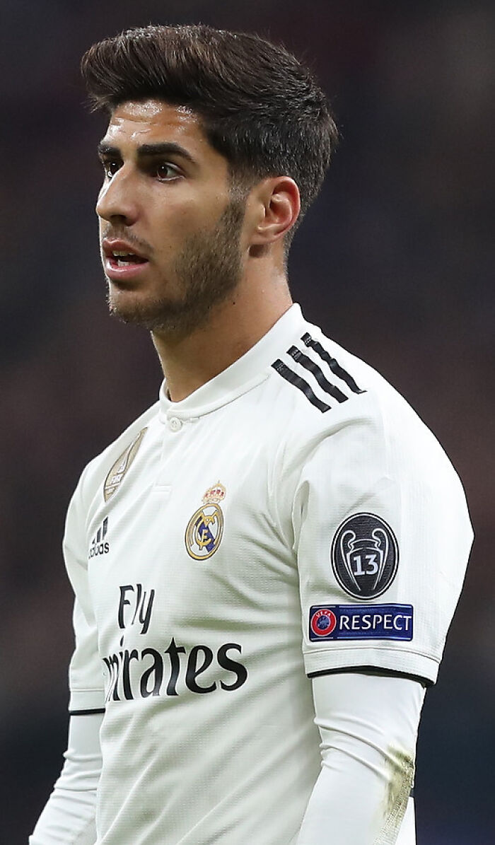 Marco Asensio in a white Real Madrid jersey during a match, focused and showing determination on the field.