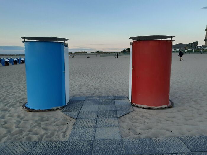 Two gendered beach changing cabins in blue and red standing on sandy beach at sunset, illustrating gendered nonsense.