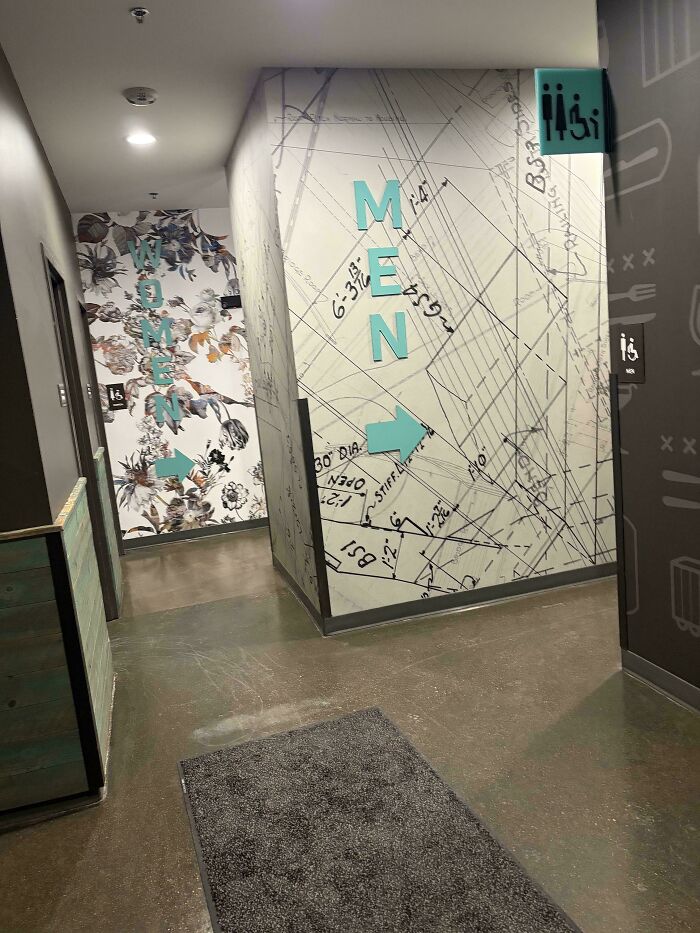 Restroom hallway with gendered nonsense signs for men and women, featuring floral and technical wall designs.